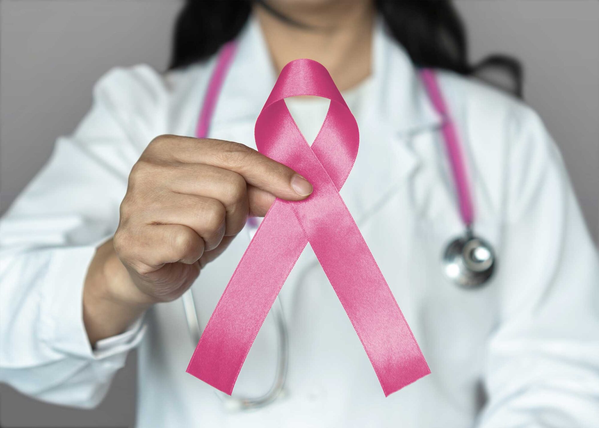 Woman in lab coat holds pink breast cancer awareness ribbon